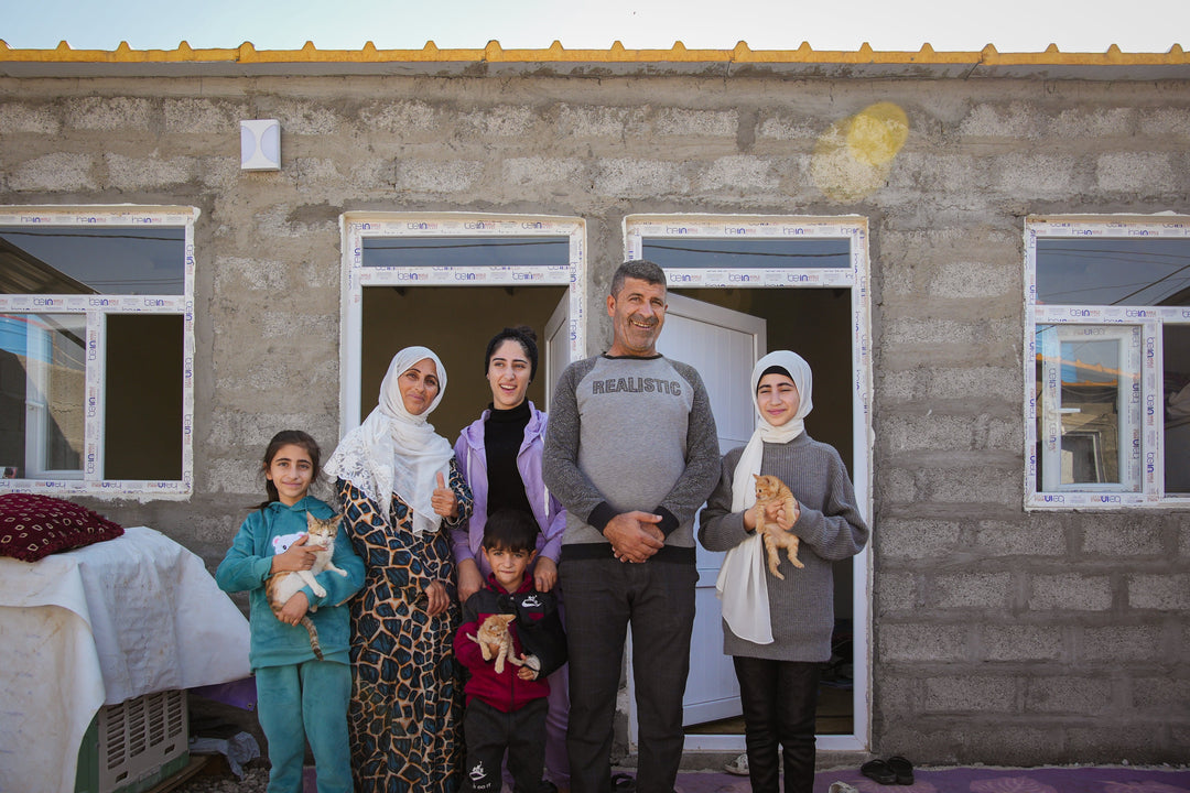 Den syriska familjen i artikeln framför sitt nya hus. Tre av barnen bär varsin katt.