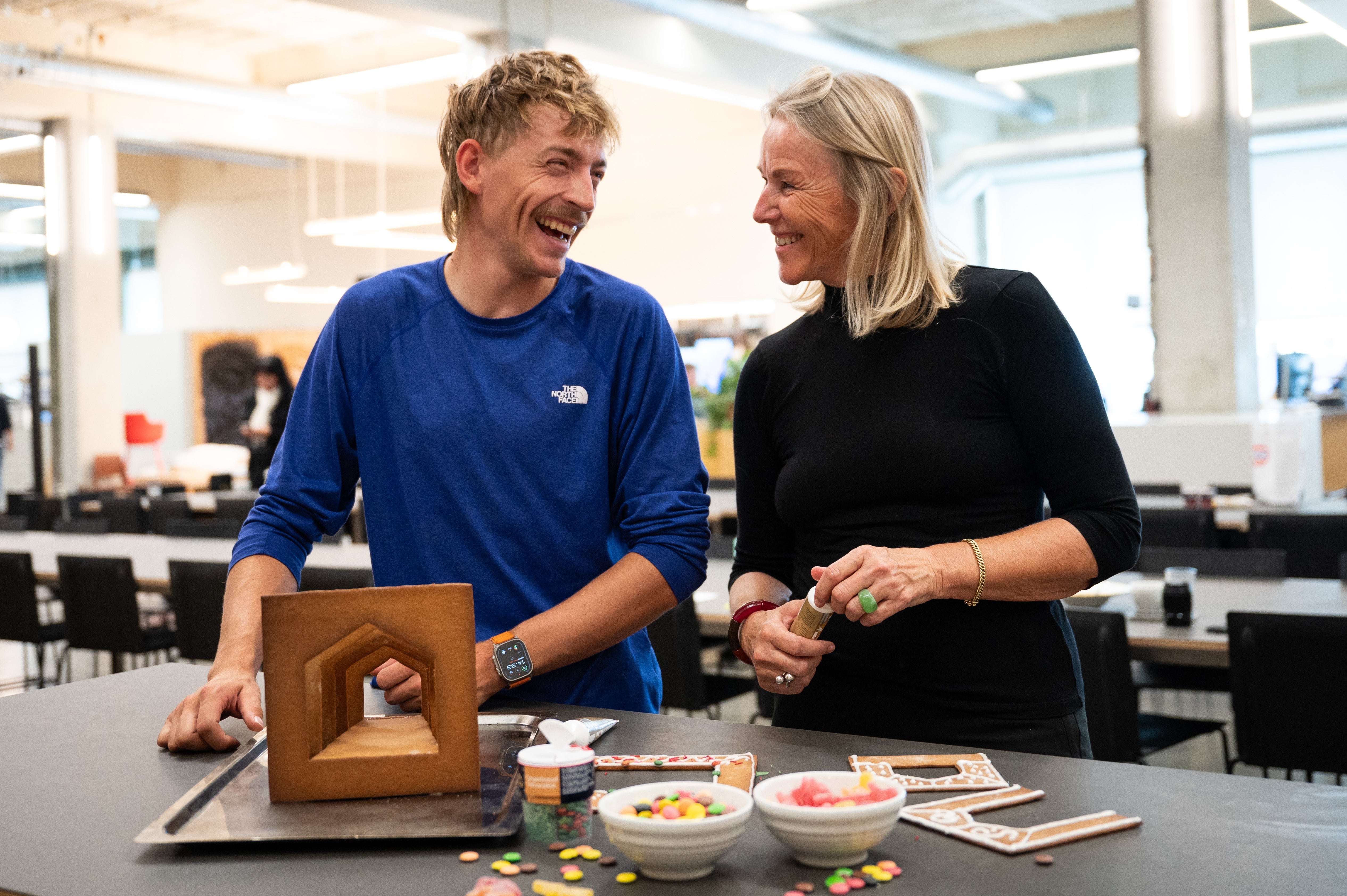 Praktikanten Clemens Rath och arkitekten Ingebjørg Skaare från Snøhetta dekorerar glatt delar av pepparkakshuset "Hemmet som är borta" tillsammans, med kristyr och godis. En odekorerad version av huset står också uppbyggd framför Clemens.