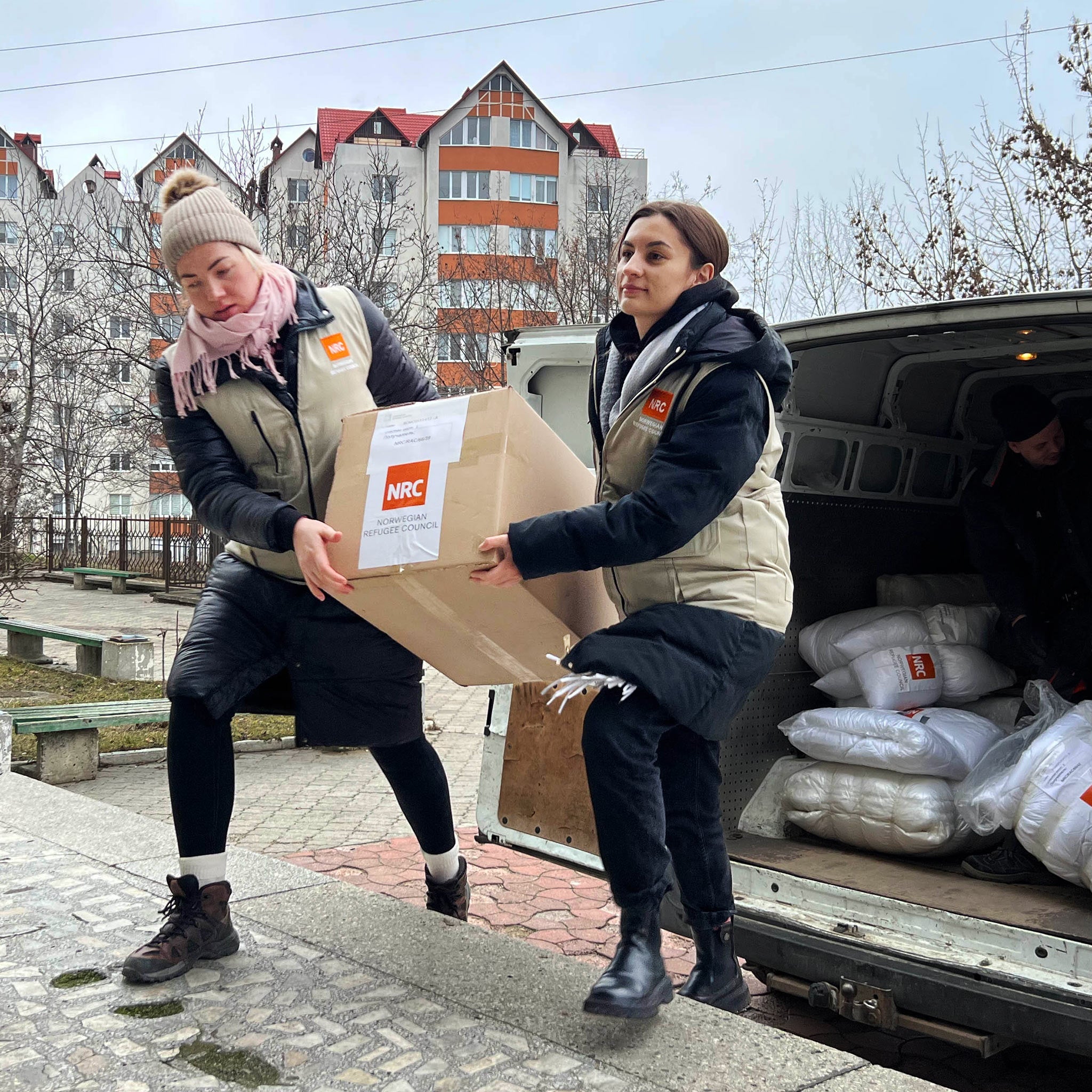 Två hjälparbetare, anställda hos NRC i Moldavien, bär en låda med NRC:s logotyp på från en mindre lastbil. I bilen finns mer vinternödhjälp till människor på flykt, redo att lastas av.