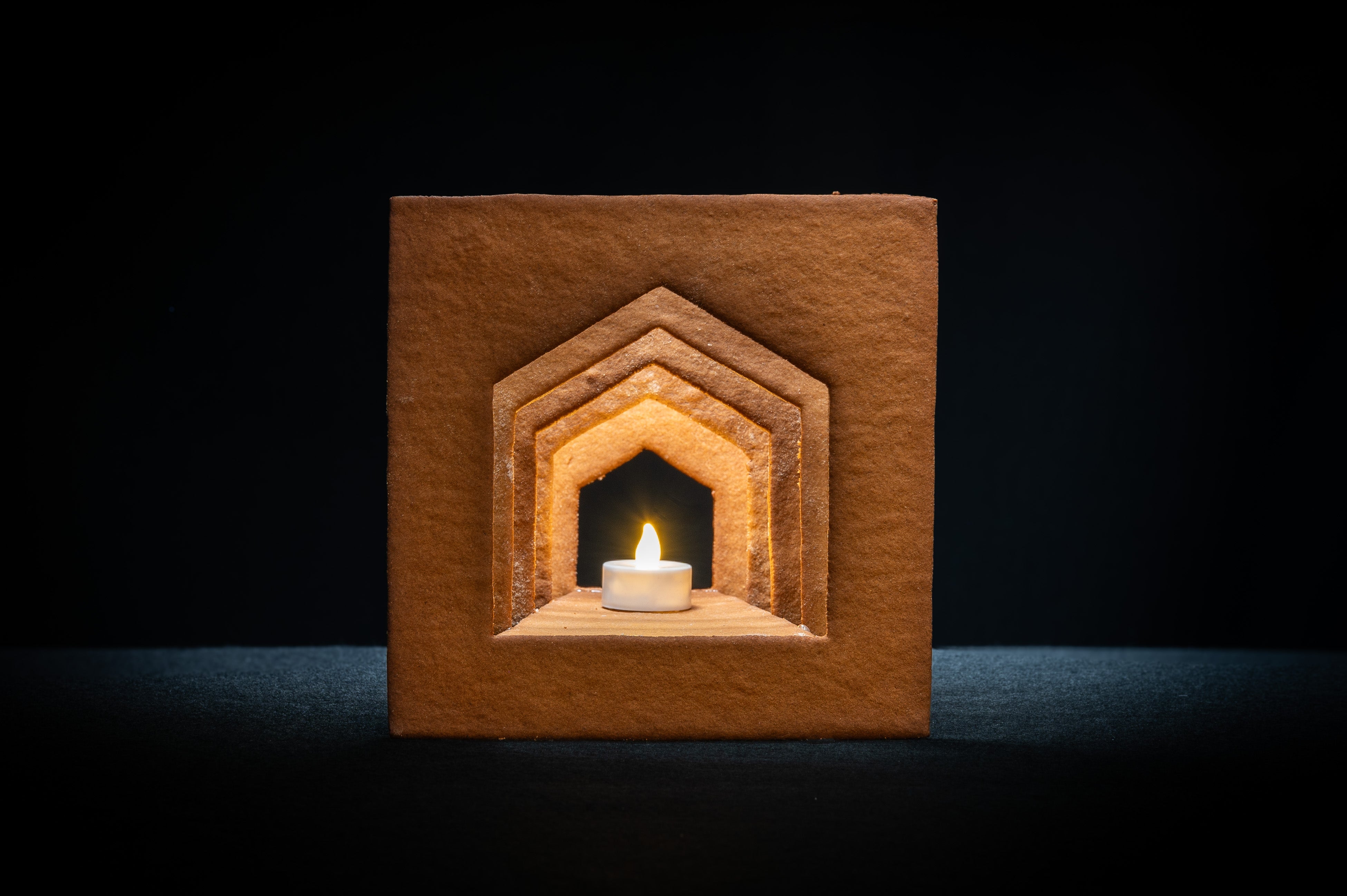 Det färdigbyggda pepparkakshuset ”Hemmet som är borta” sett framifrån, odekorerat och med ett tänt led-ljus placerat i huset.