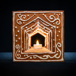 Det färdigbyggda pepparkakshuset ”Hemmet som är borta”, dekorerat med snirklig kristyr och med ett tänt led-ljus placerat i huset.