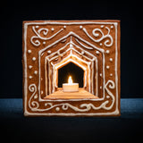 Det färdigbyggda pepparkakshuset ”Hemmet som är borta”, dekorerat med snirklig kristyr och med ett tänt led-ljus placerat i huset.