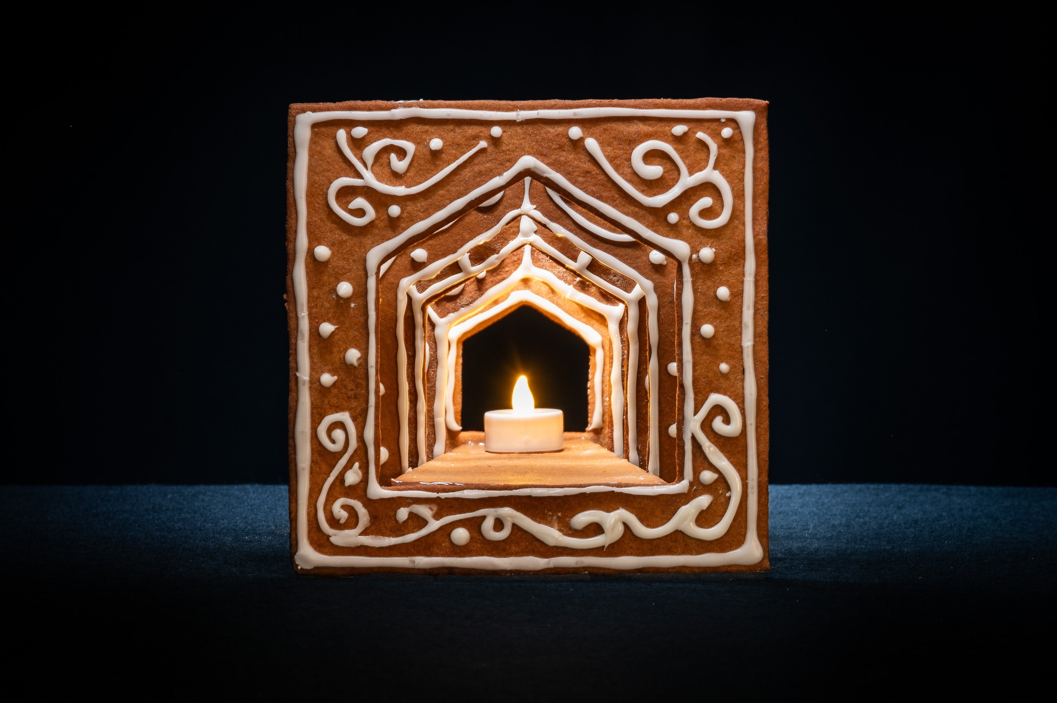 Det färdigbyggda pepparkakshuset ”Hemmet som är borta”, dekorerat med snirklig kristyr och med ett tänt led-ljus placerat i huset.