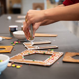 En person dekorerar delar av pepparkakshuset ”Hemmet som är borta” med kristyr.