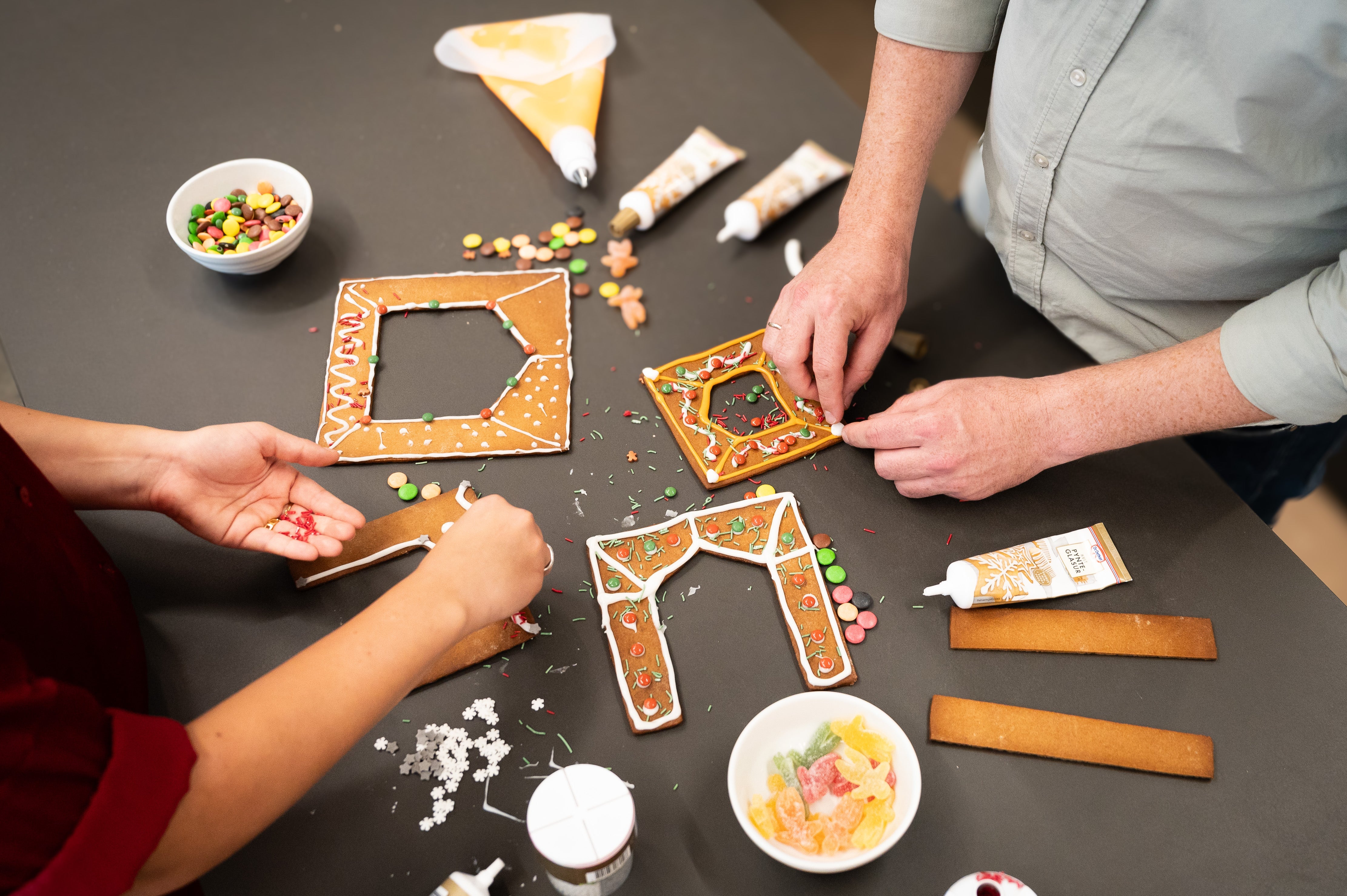 Två personer dekorerar delar av pepparkakshuset ”Hemmet som är borta” med godis.